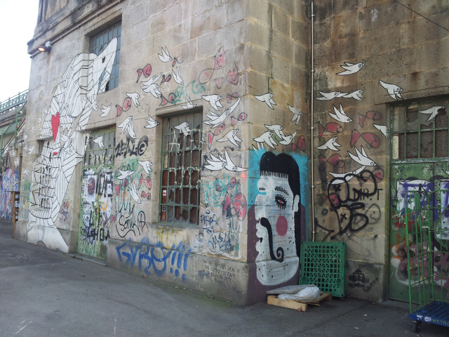 Ein Picasso-eskes Gesicht und Vögel entlang einer Hausmauer am Kanal.